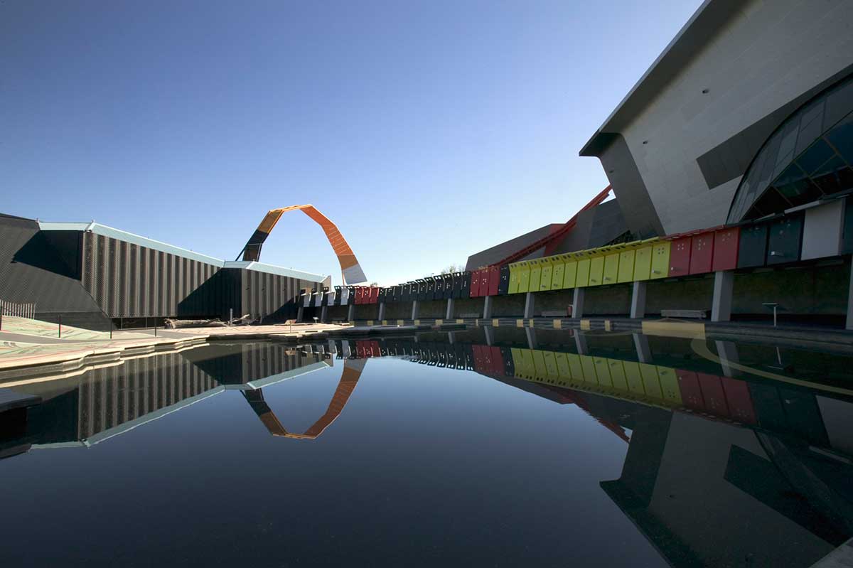 A tranquil setting in an outdoor museum space featuring a giant sculptural loop reflected in a body of water. 