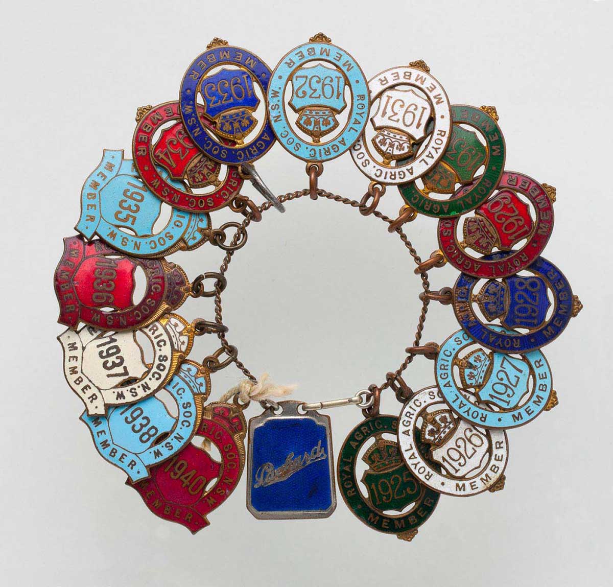 Fifteen Royal Agricultural Society Member Badges dated from 1925 to 1938 and 1940, and a Packard key ring, attached to a metal link chain. - click to view larger image