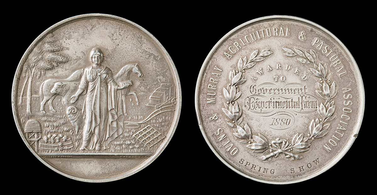 Photo of two circular medal faces, side by side. The face on the left has a raised image of a classical figure standing in a rural/industrial scene. - click to view larger image