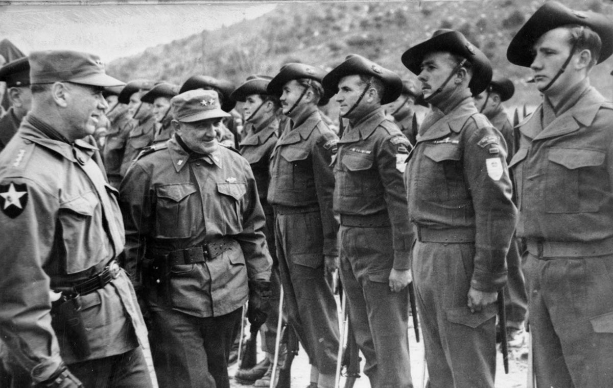 A short, smiling man in his fifties or sixties in Army uniform inspects Australian soldiers standing at attention