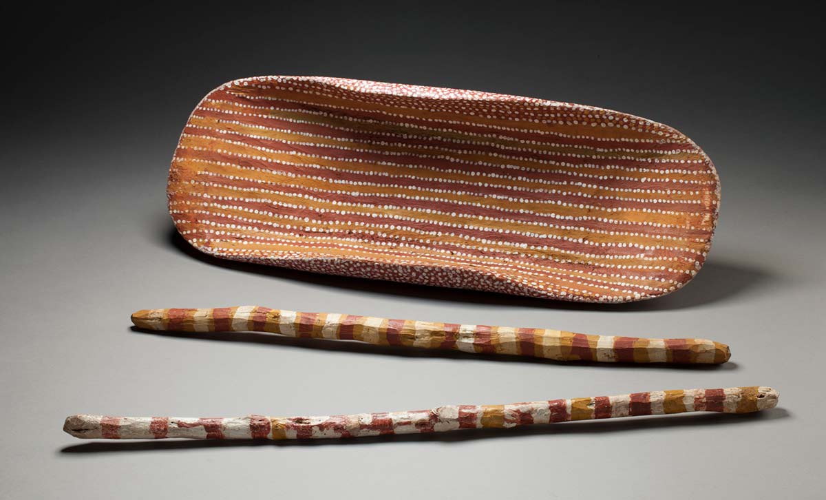 A coolamon painted in red and orange stripes which are outlined in white dots. There is also one green stripe also outlined in white dots. - click to view larger image