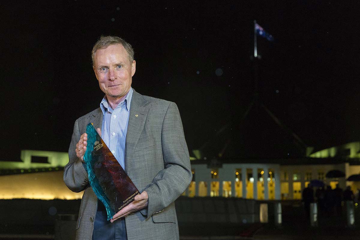 A photo of a man holding a trophy, outside at night.