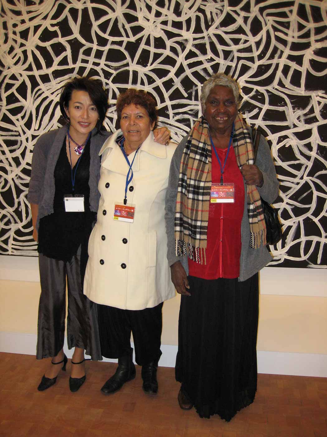Three women standing in front of a large painting. - click to view larger image