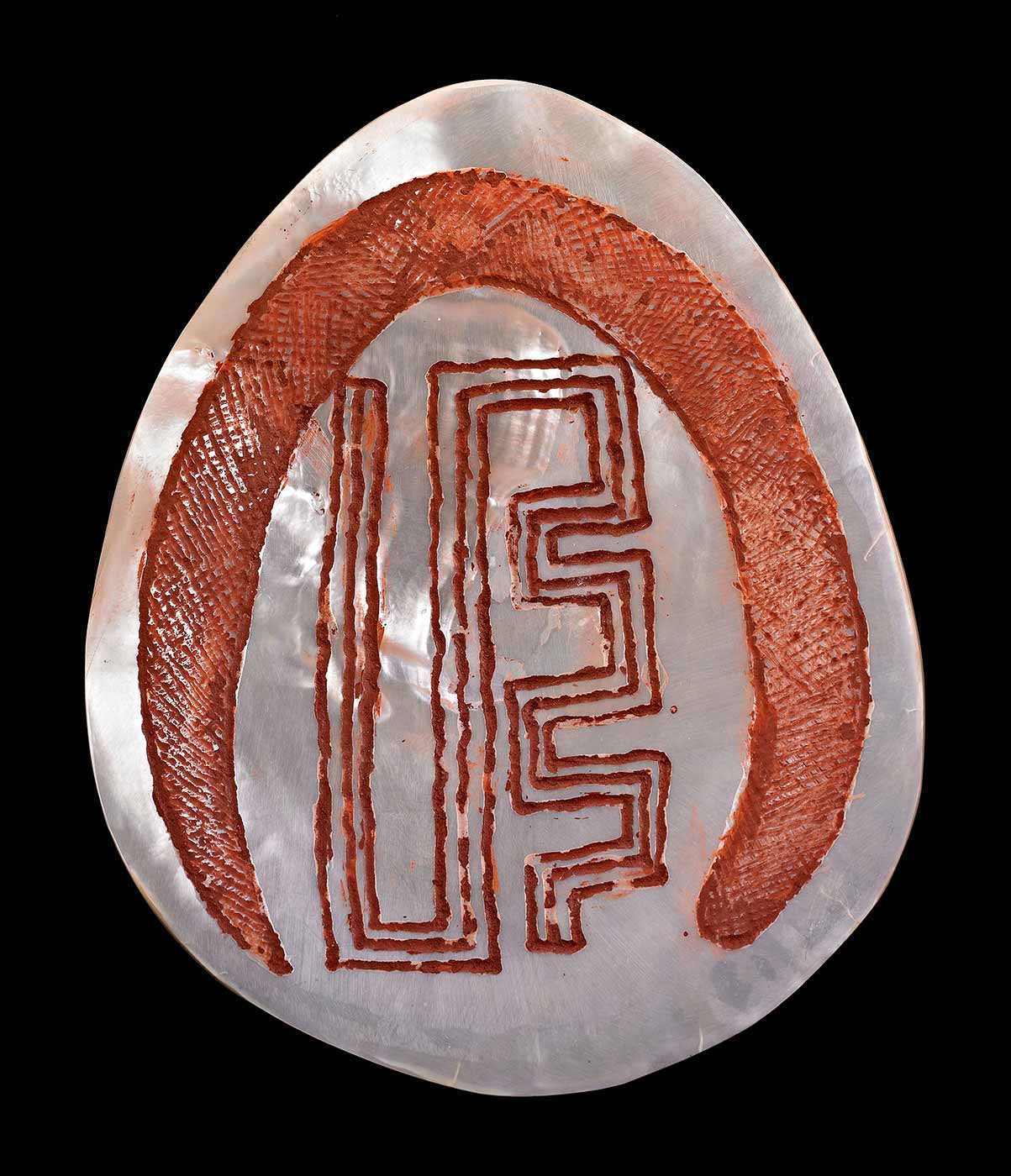 Ornament made from carved and polished pearlshell. Incised with the design of the Rainbow Serpent with red ochre filling the incisions.