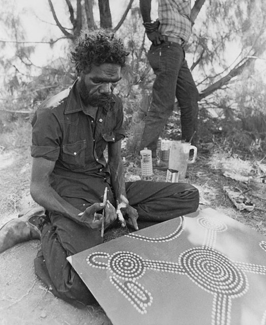 Aboriginal Australian man sitting on the ground painting a canvas. - click to view larger image