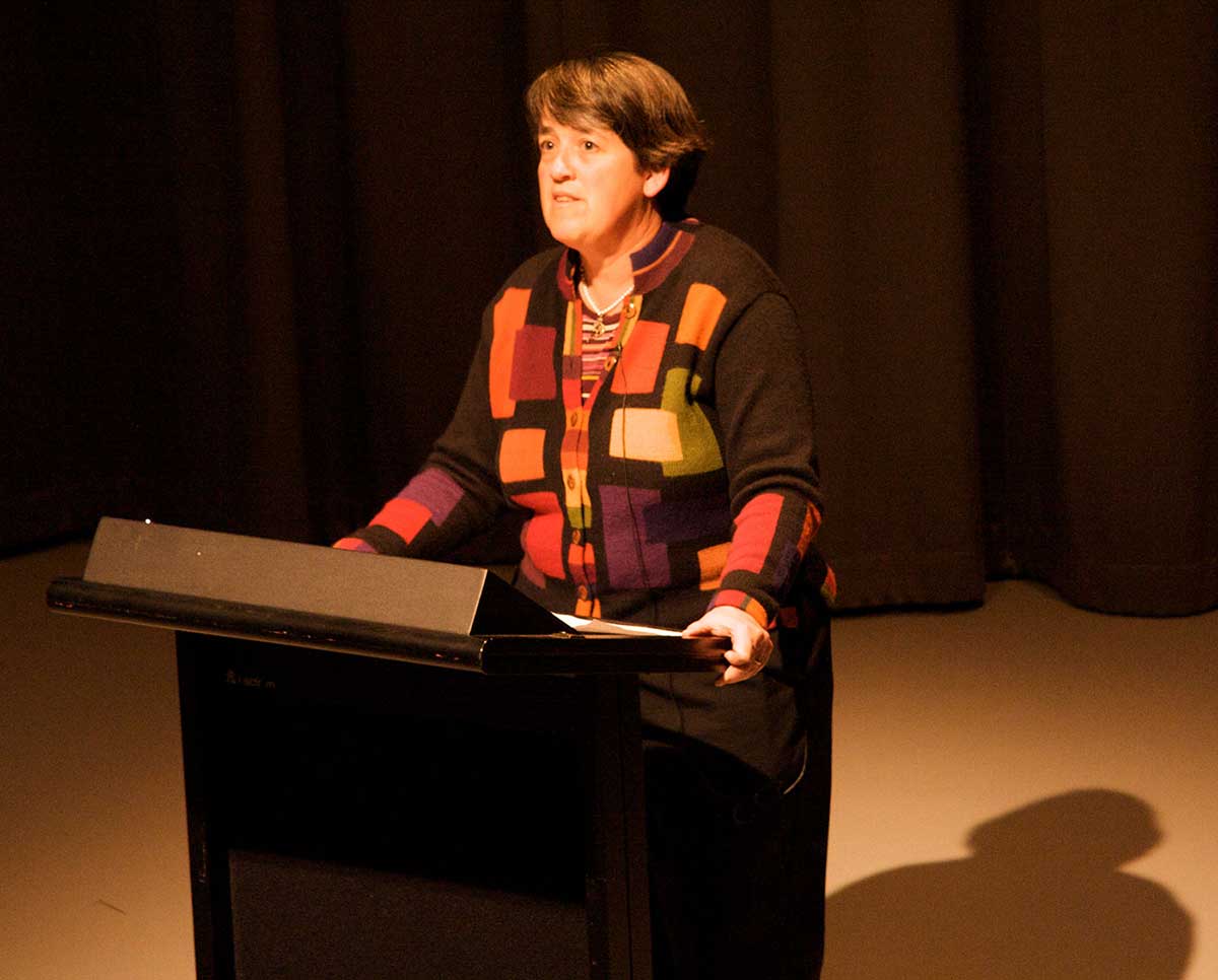 A woman stands at a lectern on a stage. - click to view larger image