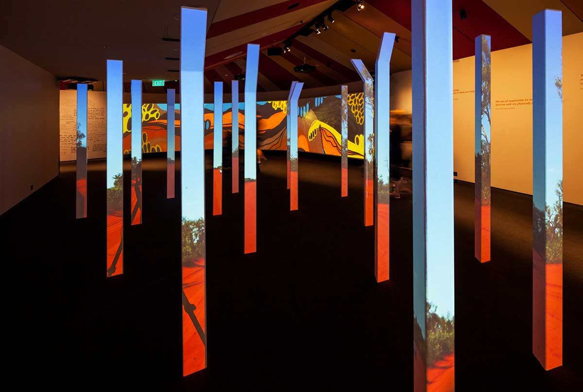 A gallery space in a museum featuring an image of a landscape projected onto a series of poles.
