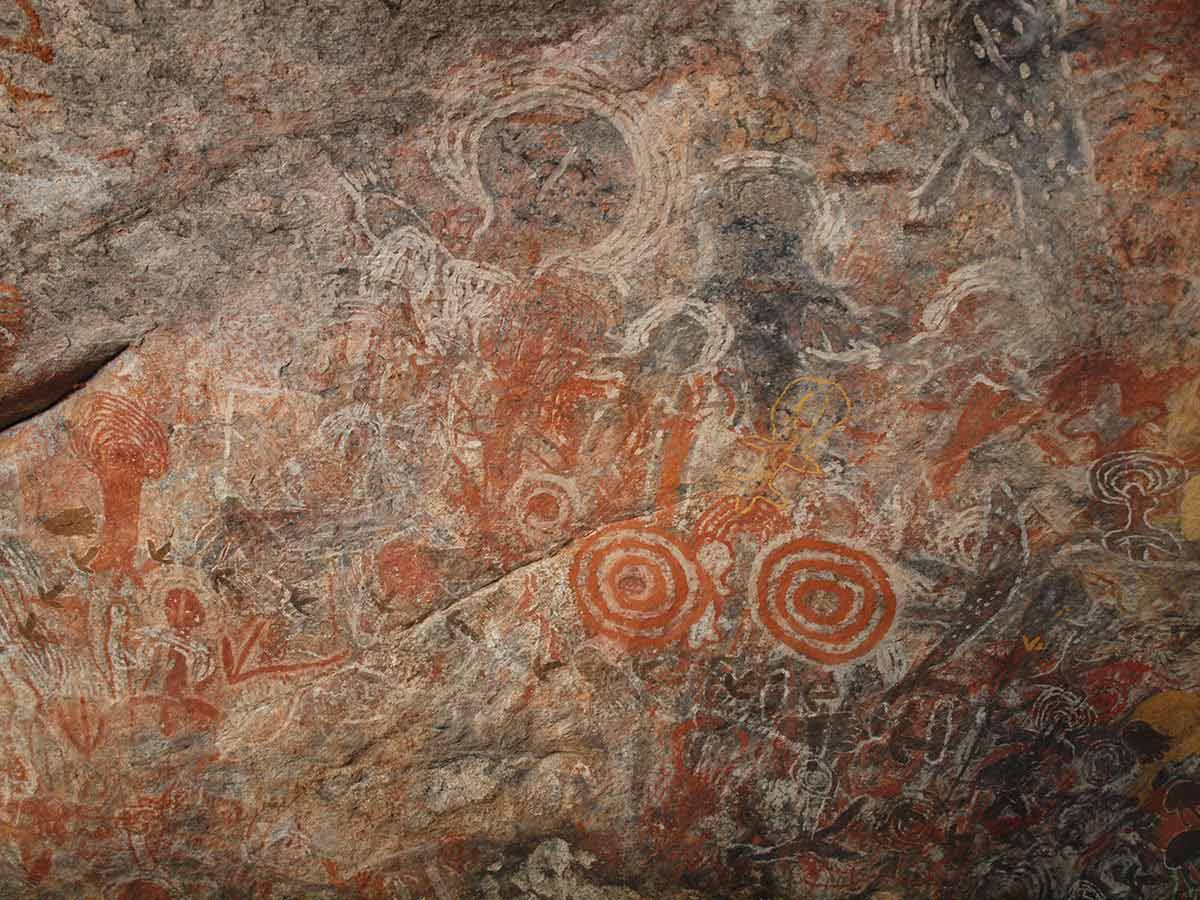 Rock art including human forms, animal tracks and concentric circles, painted in shades of ochre.