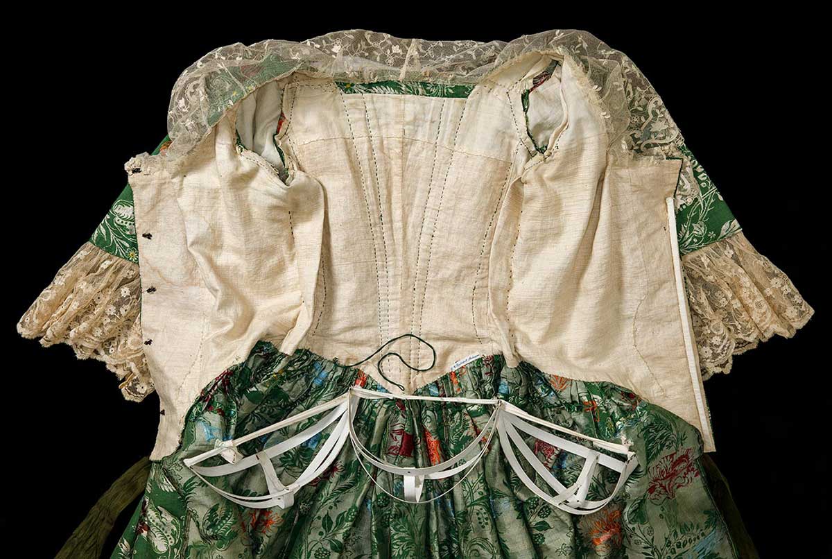 Green and floral brocade open-front robe features lace trim on sleeves and collar, and three small fabric-covered metal panniers. - click to view larger image