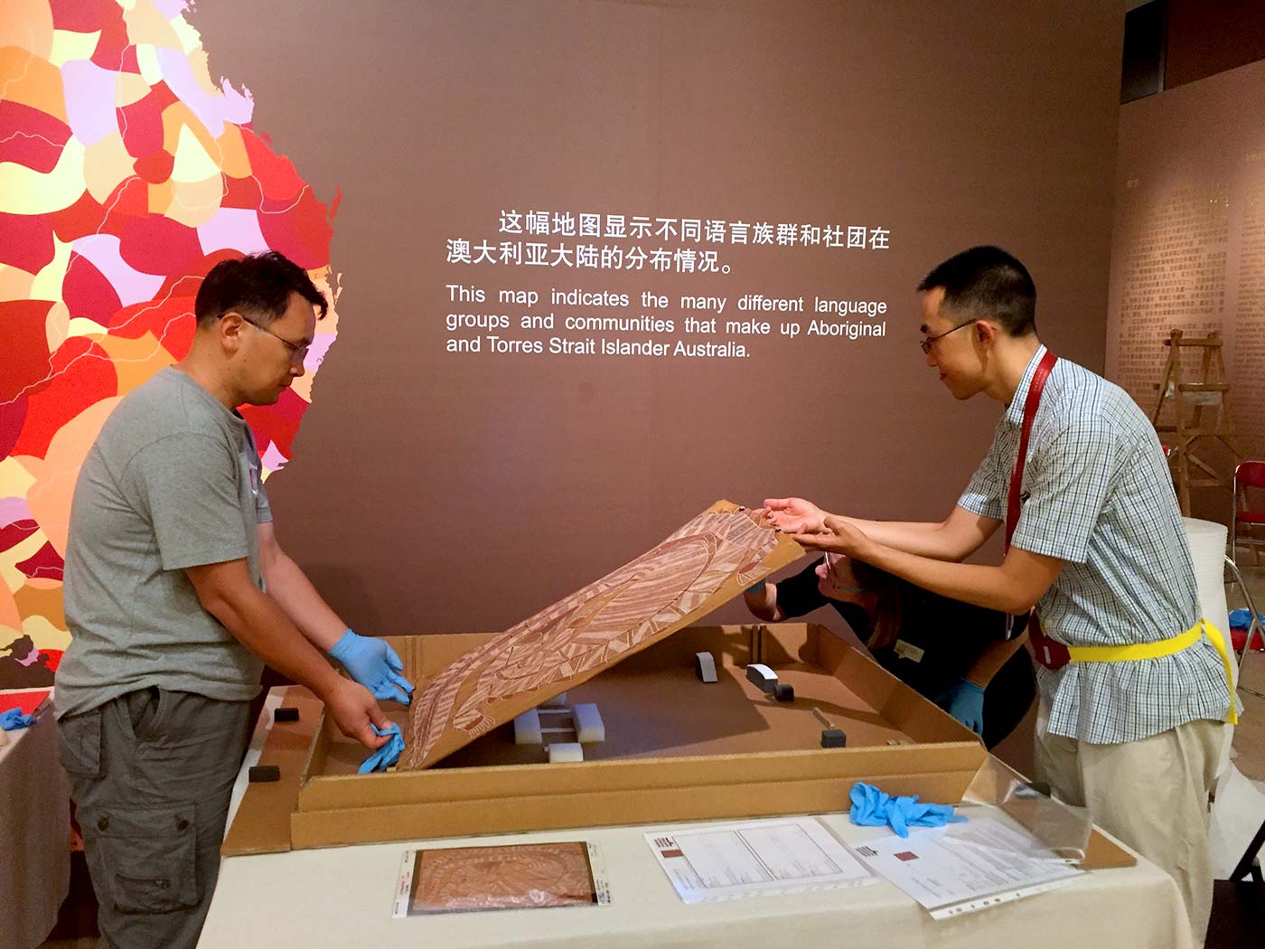 Museum staff lift a bark painting from its transportation box.