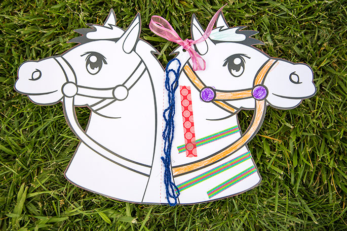 A paper template of a horse's head which has been folded in half so that there is a head on either side. One side has been decorated.