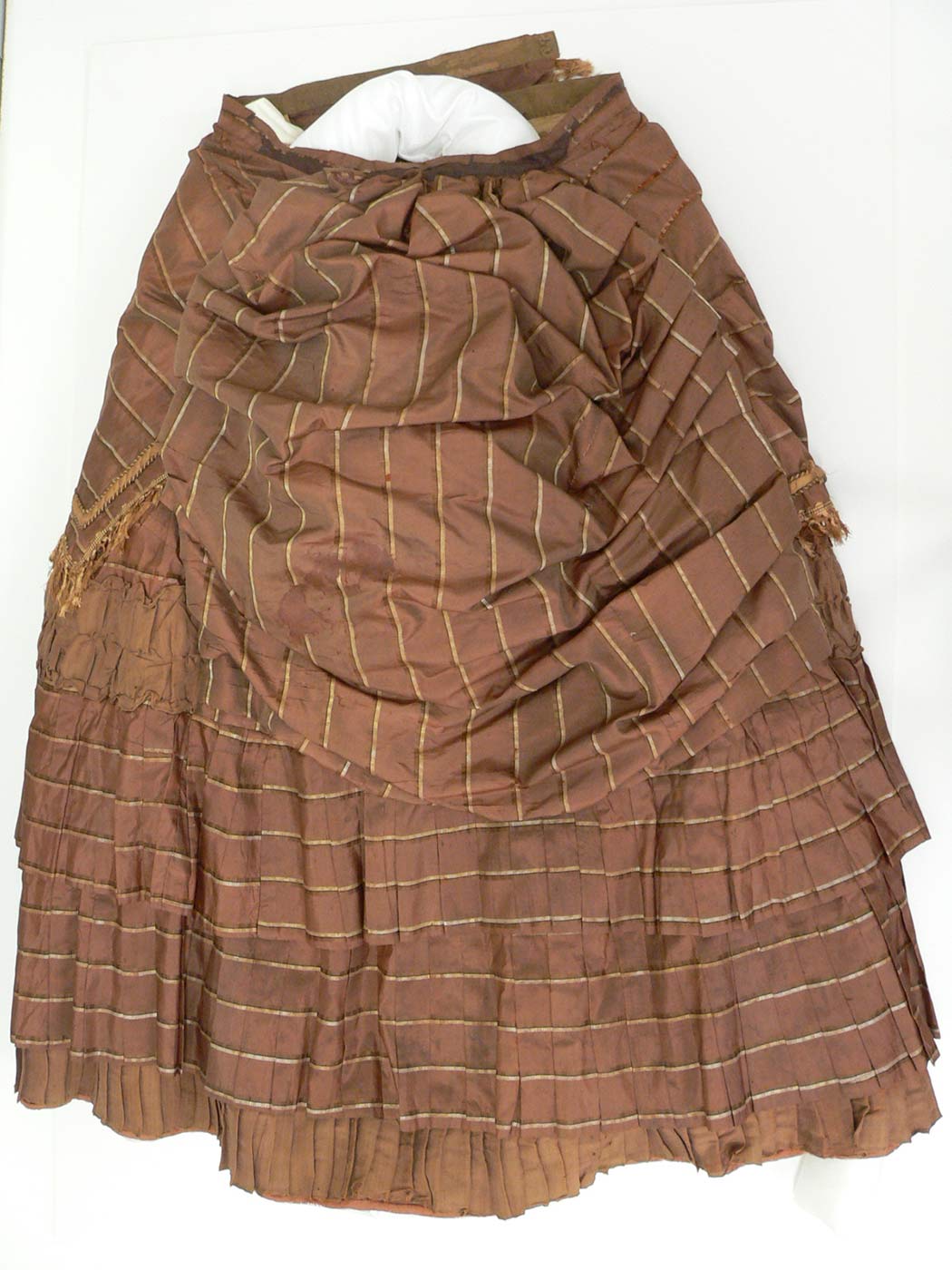 Colour photograph of a skirt of flat rust brown silk woven with figured stripes of brown and cream fabric.  - click to view larger image