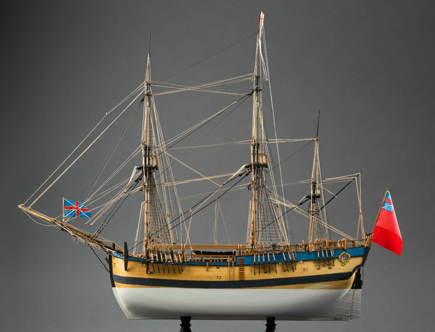 Side view of a model wooden sailing ship with a red flag at the rear. - click to view larger image