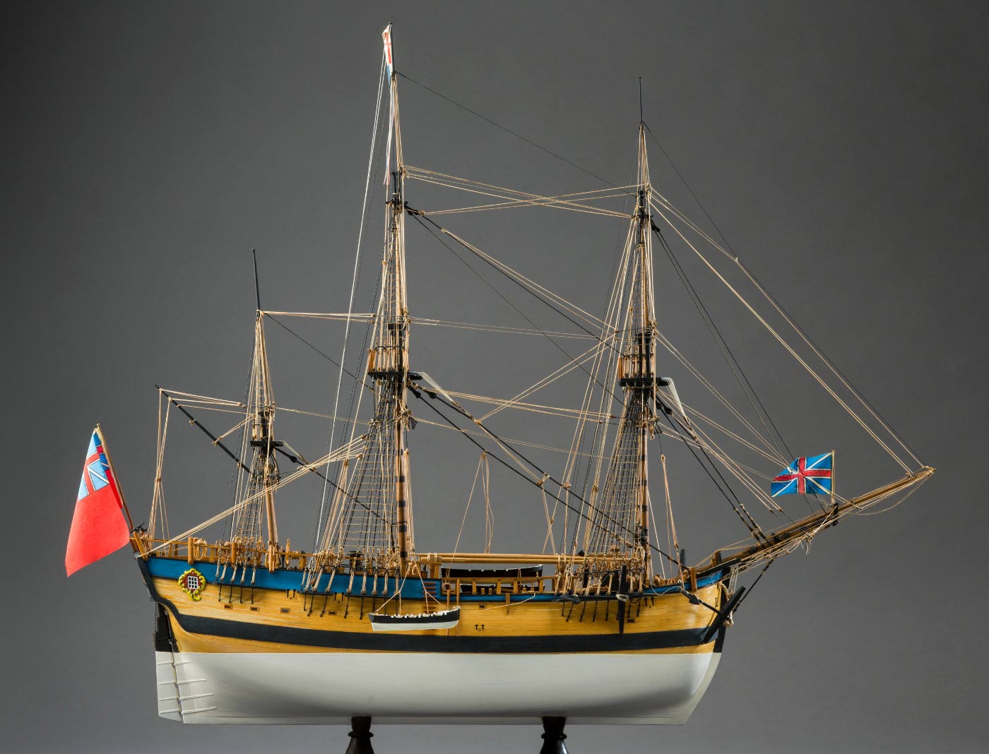 Side view of a model wooden sailing ship with a small boat partially lowered over the side. - click to view larger image