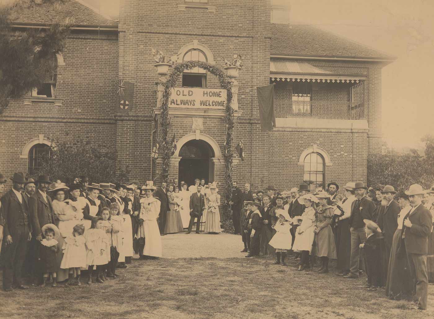 Springfield homestead decorated with a floral archway, flags and a banner 'OLD HOME ALWAYS WELCOME'. The Faithfull family and station staff stand around newly weds William Hugh and Lilian Anderson, 1898. - click to view larger image