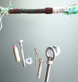 A set of chimes made from a stick wrapped in wool and string that has a variety of bolts and screws dangling from it.