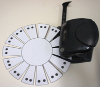 A photograph of a hole-punch placed over black dots on a sample basket template.