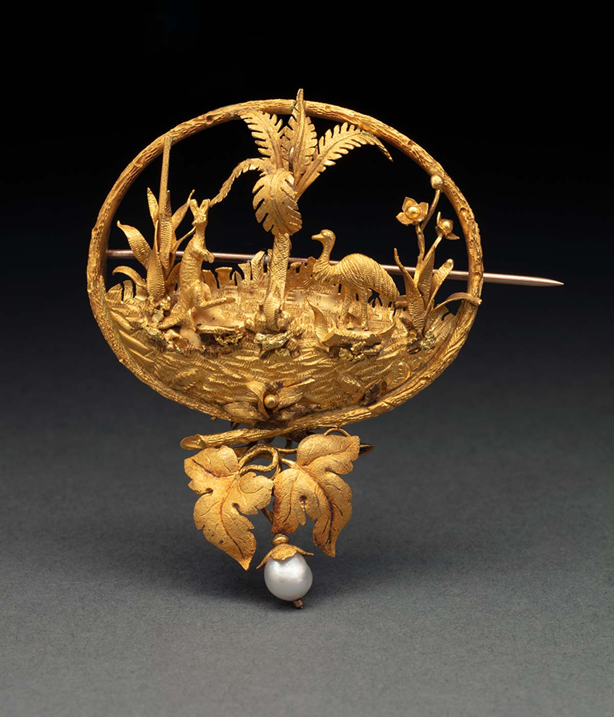 Gold brooch showing a picture of a kangaroo and emu, with a pearl drop at the bottom. - click to view larger image