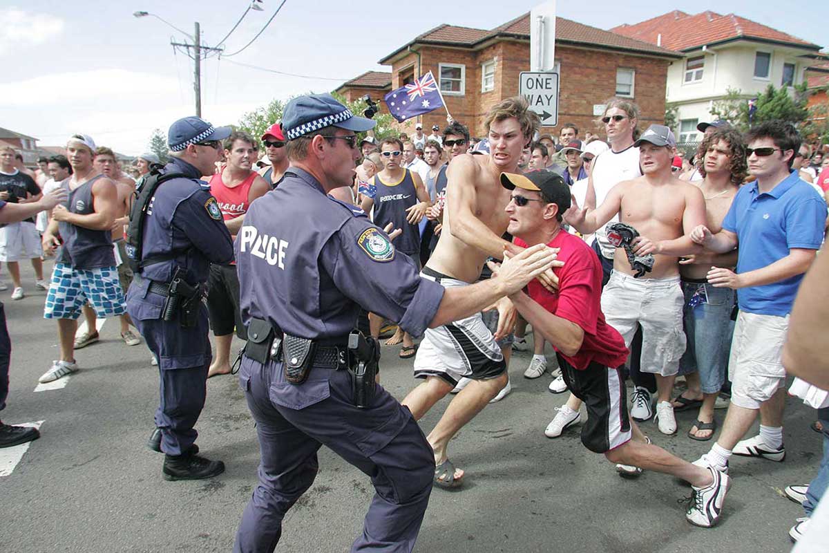 Colour photograph of police trying to hold back a large crowd of angry predominantly young white male protesters on a street.