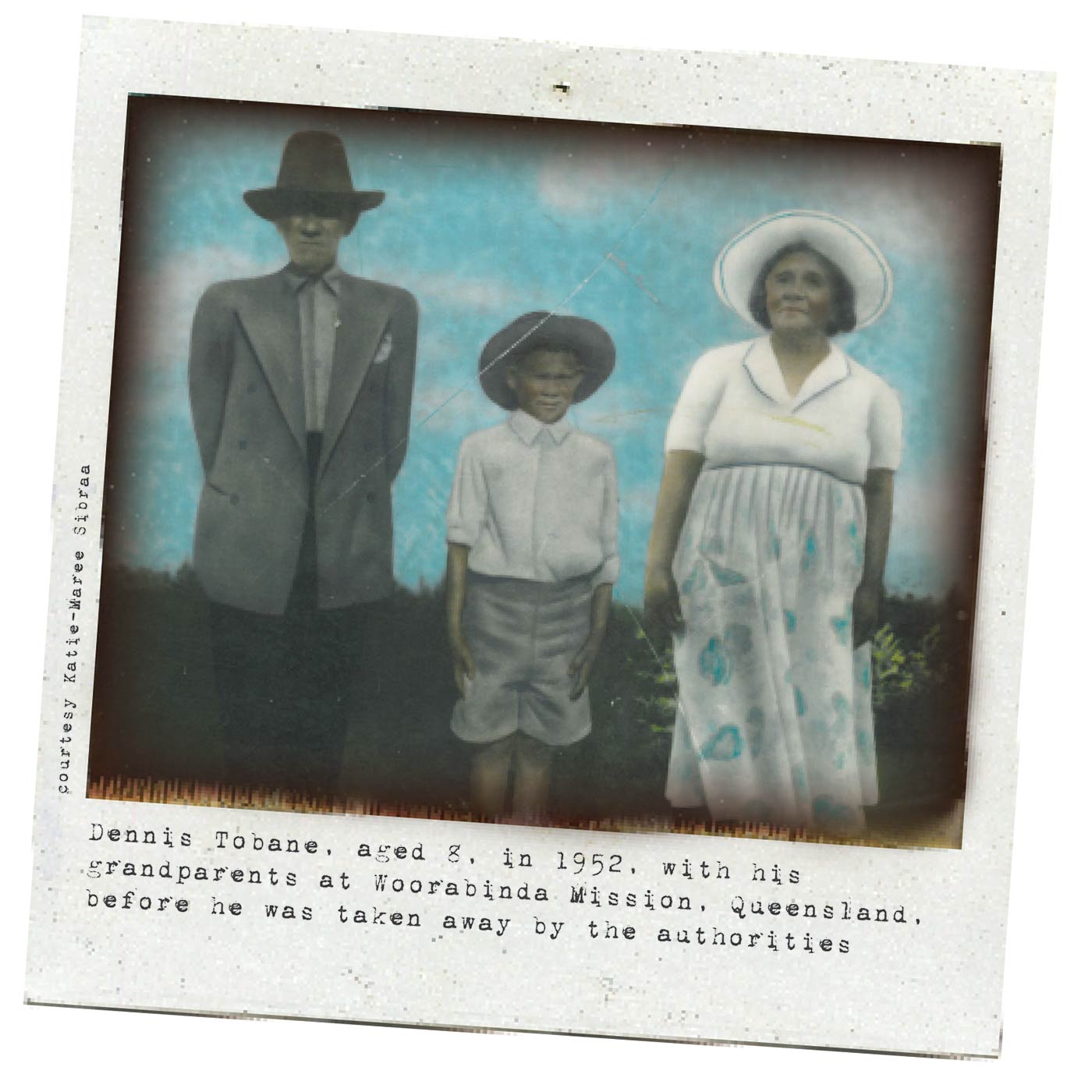A black and white Polaroid photograph portraying three people in a standing position. From left to right, there is an elderly man wearing dark trousers with a light grey blazer, shirt and hat; a young boy who has his hands firmly by his side - he is also wearing a hat - and an elderly woman wearing a light coloured skirt, white shirt and a white hat. Typewritten text underneath reads: 'Dennis Tobane, aged 8, in 1952, with his grandparents at Woorabinda Mission, Queensland, before he was taken away by the authorities'. In smaller text, on the left-hand side of the image, in a vertical direction, reads: 'Courtesy Katie-Maree Sibraa.' - click to view larger image