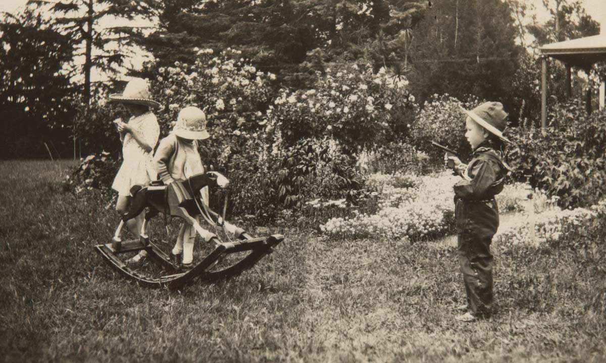 Black and white photograph of children playing dress ups in a garden. - click to view larger image