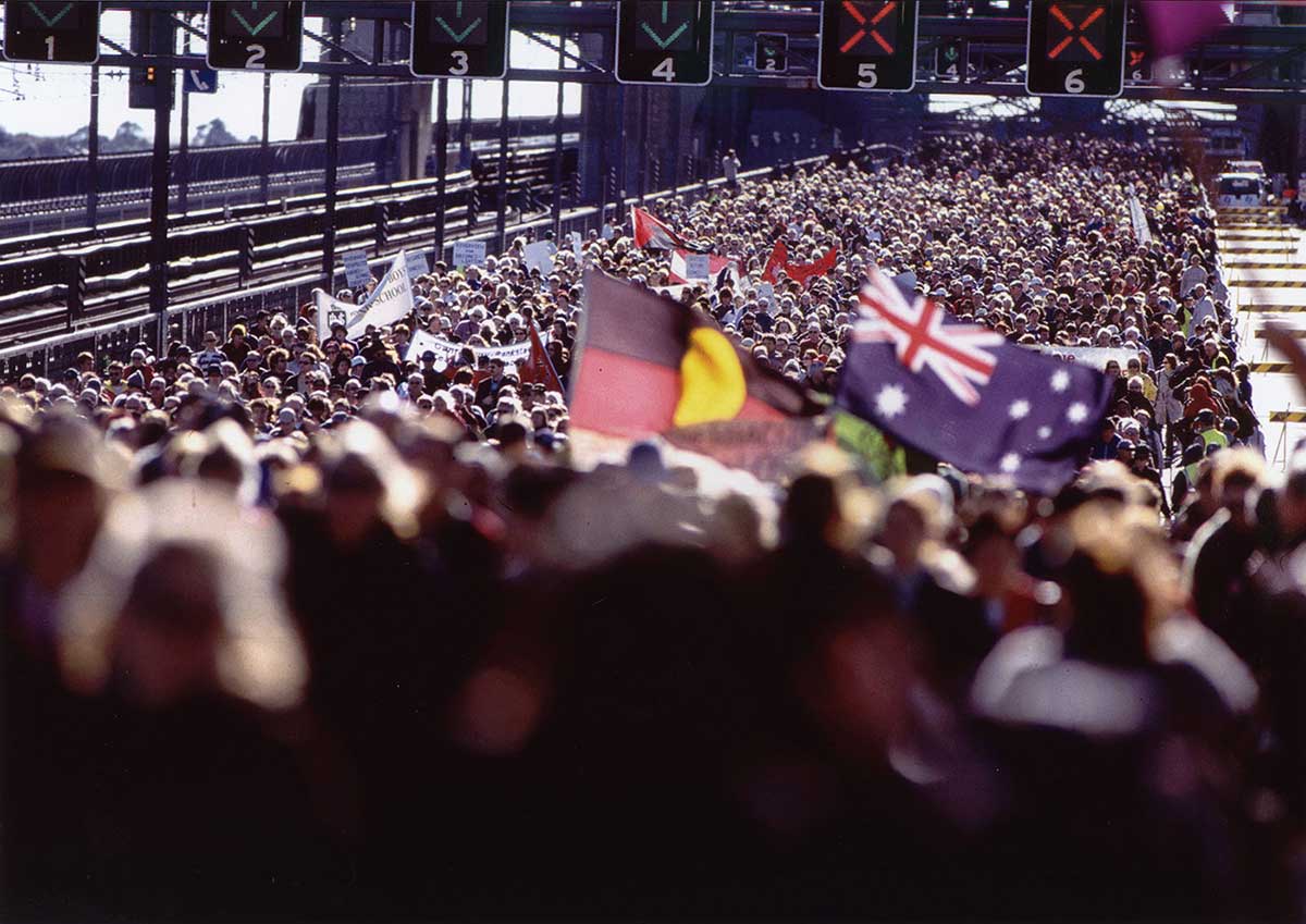 A huge crowd of people on the Sydney Harbour Bridge, with the Aboriginal flag being carried alongside the Australian flag. - click to view larger image