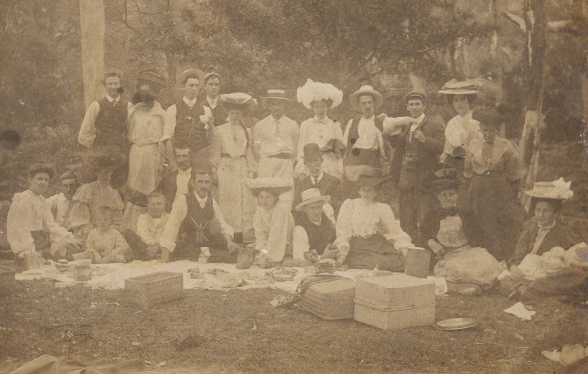 Sepia toned vignette photographic postcard featuring a group of people at a picnic. - click to view larger image