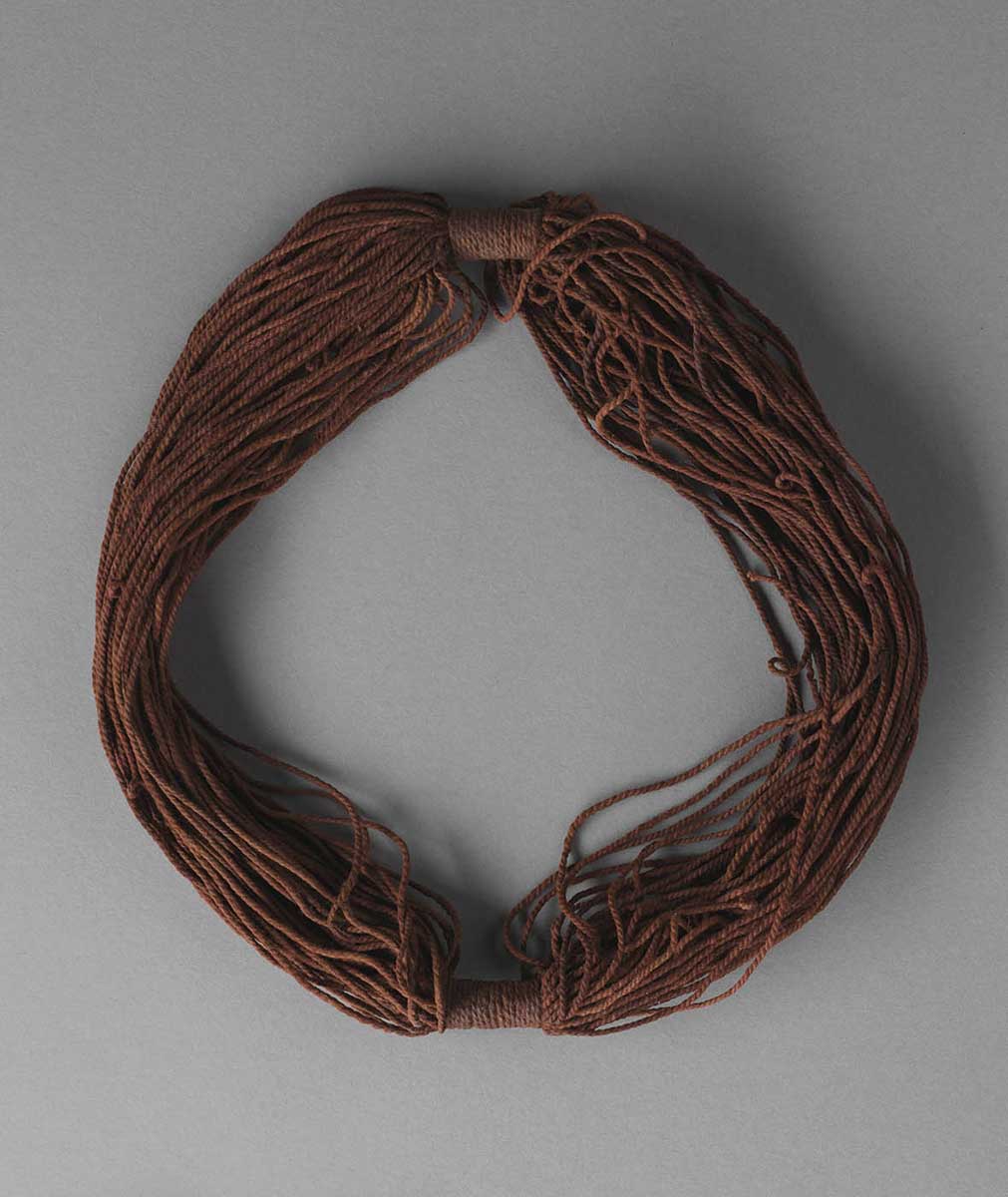 A headband, made up of multiple strands of brown-pigmented two-ply natural fibre string. The strands are gathered in at opposite sides of the headband by the same string, tied tightly across the strands. Some of the strands on the right-hand side have small loops in them. - click to view larger image