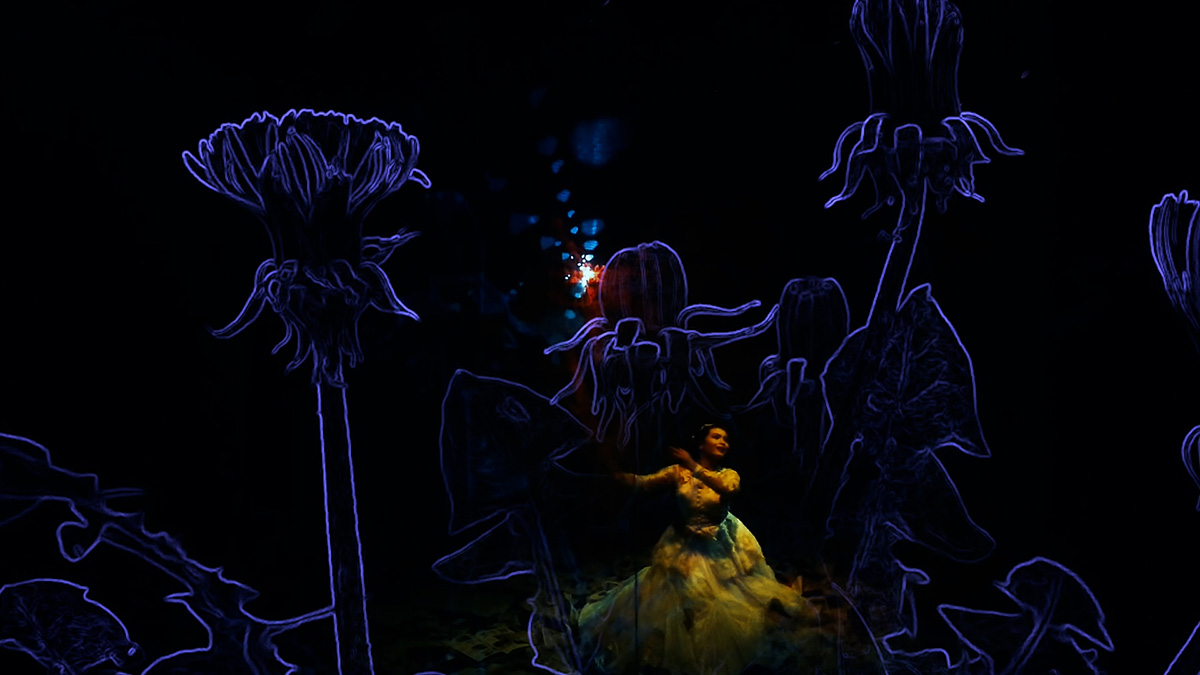 Woman on a dark stage with projections of computer-generated flowers behind her - click to view larger image