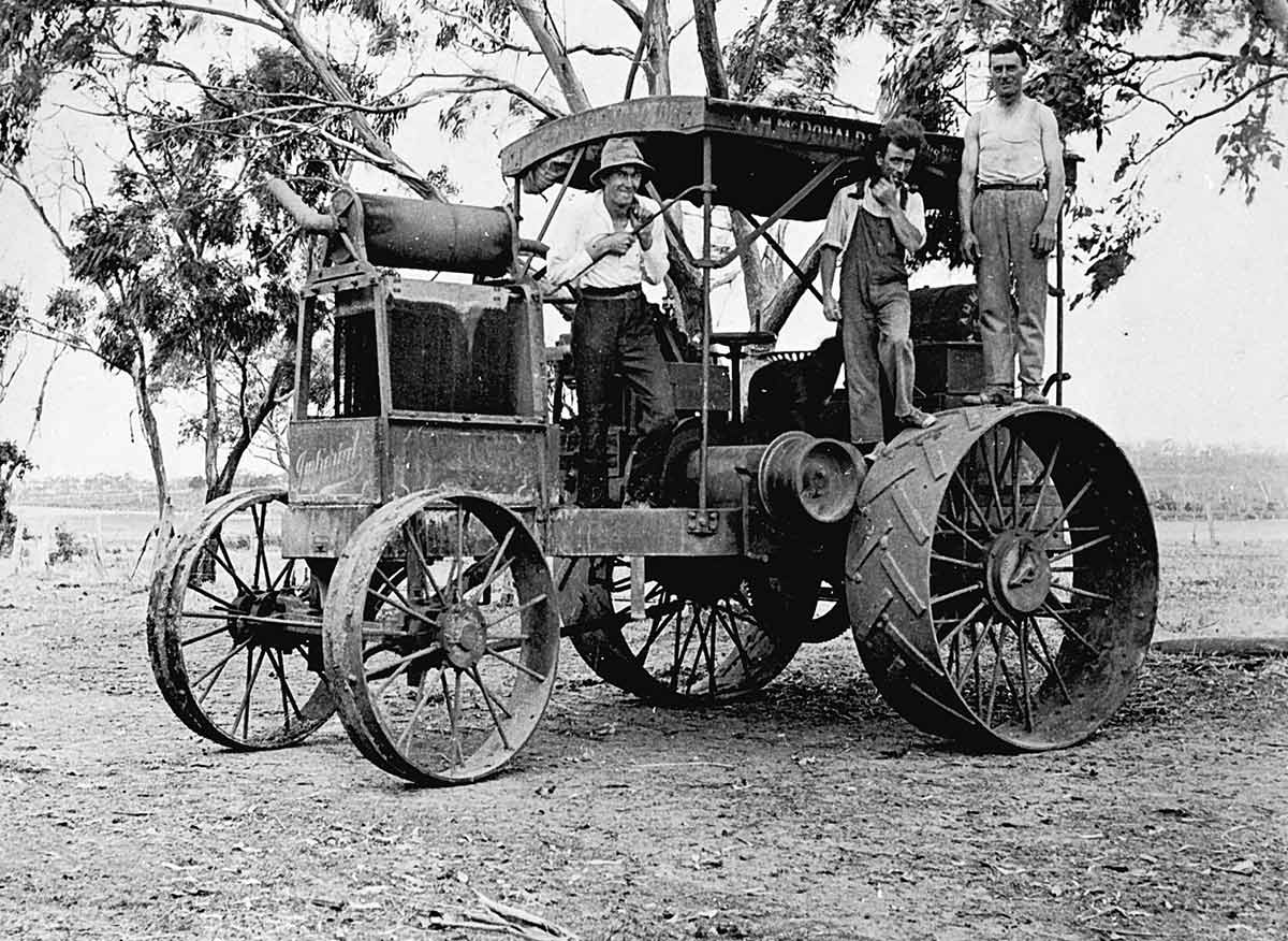 Black and white photograph of three men standing on a stationary tractor.