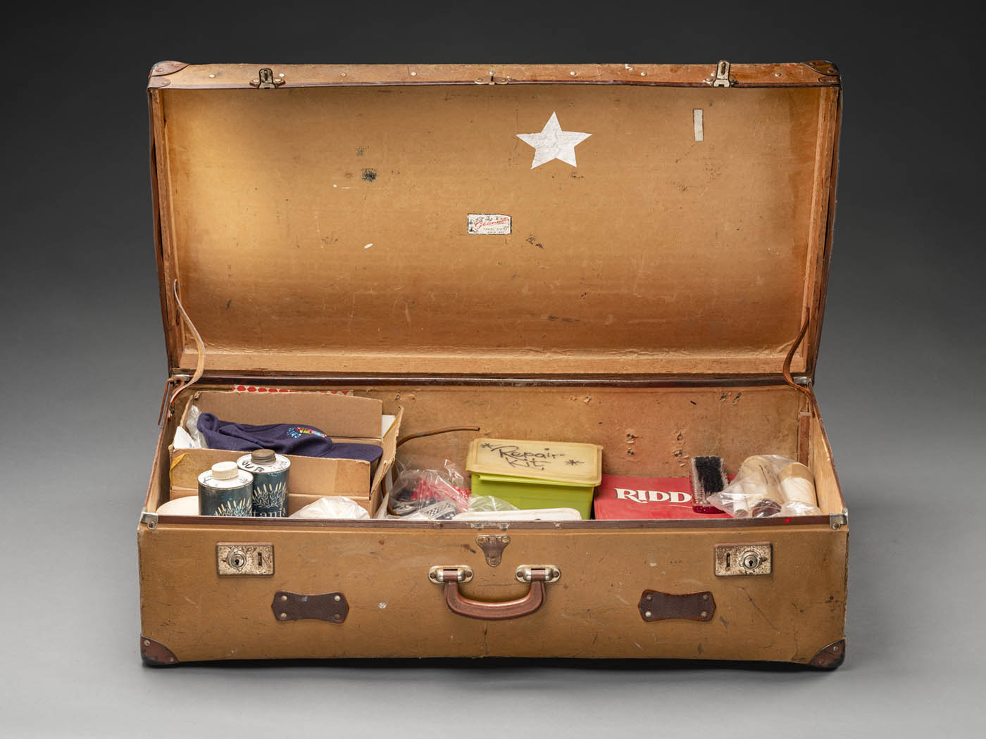 A photograph of Norman Hetherington’s suitcase which he took to the studio when recording. The suitcase is brown with a leather handle and two lockable metal latches.