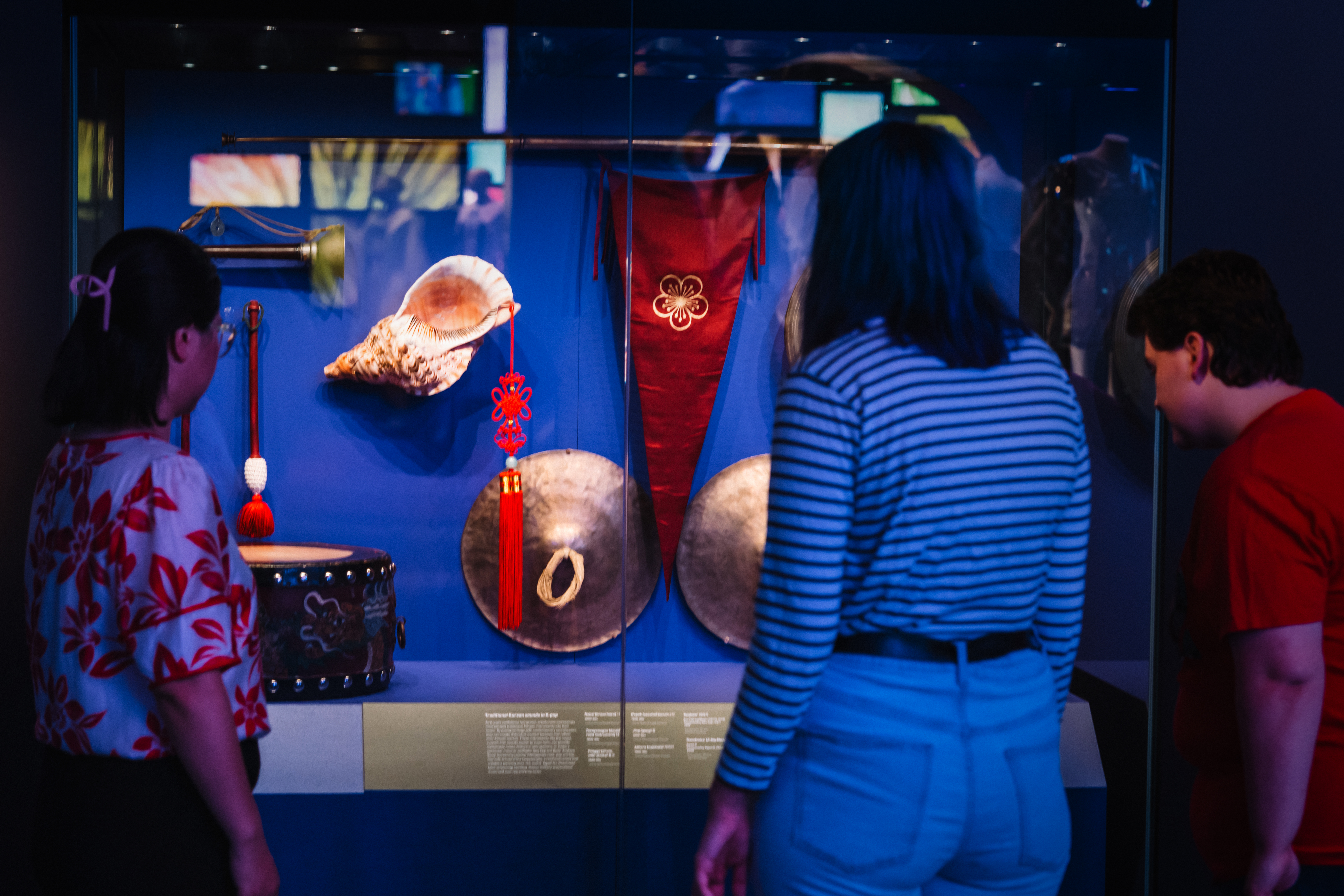 A photograph of a person looking into a museum showcase. The showcase is blue with Korean musical instruments like a horn, drum and a shell.