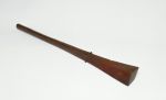 Club made of brown wood with a handle that is slightly rhomboid shaped at one end and pointed at the other. Both ends separated by a bulged ring.