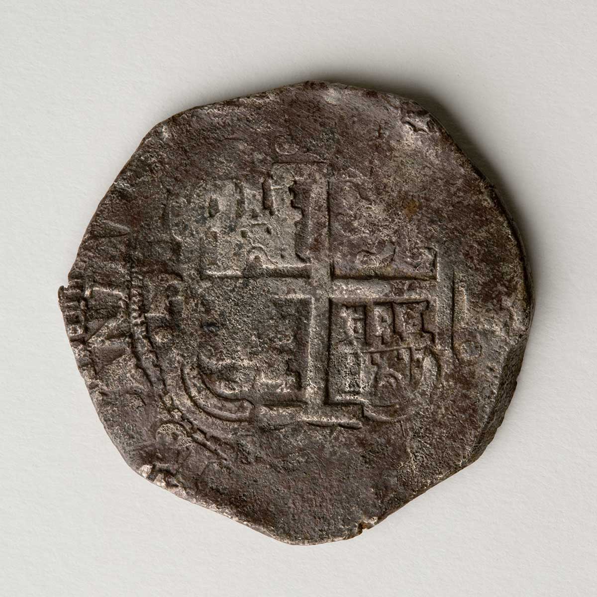Studio photo of worn and battered silver coin whose imprint is barely discernible.