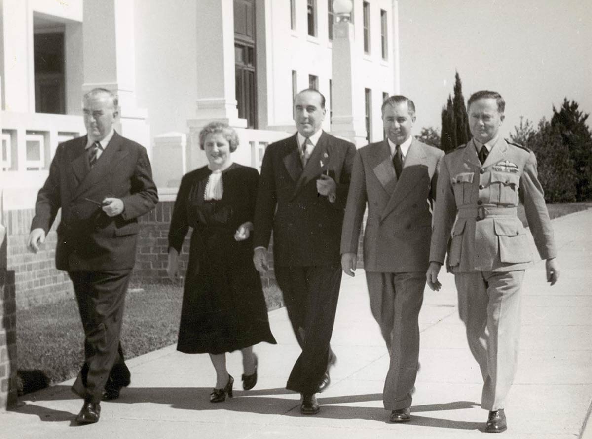Four men and a woman walking abreast along the front of Old Parliament House.