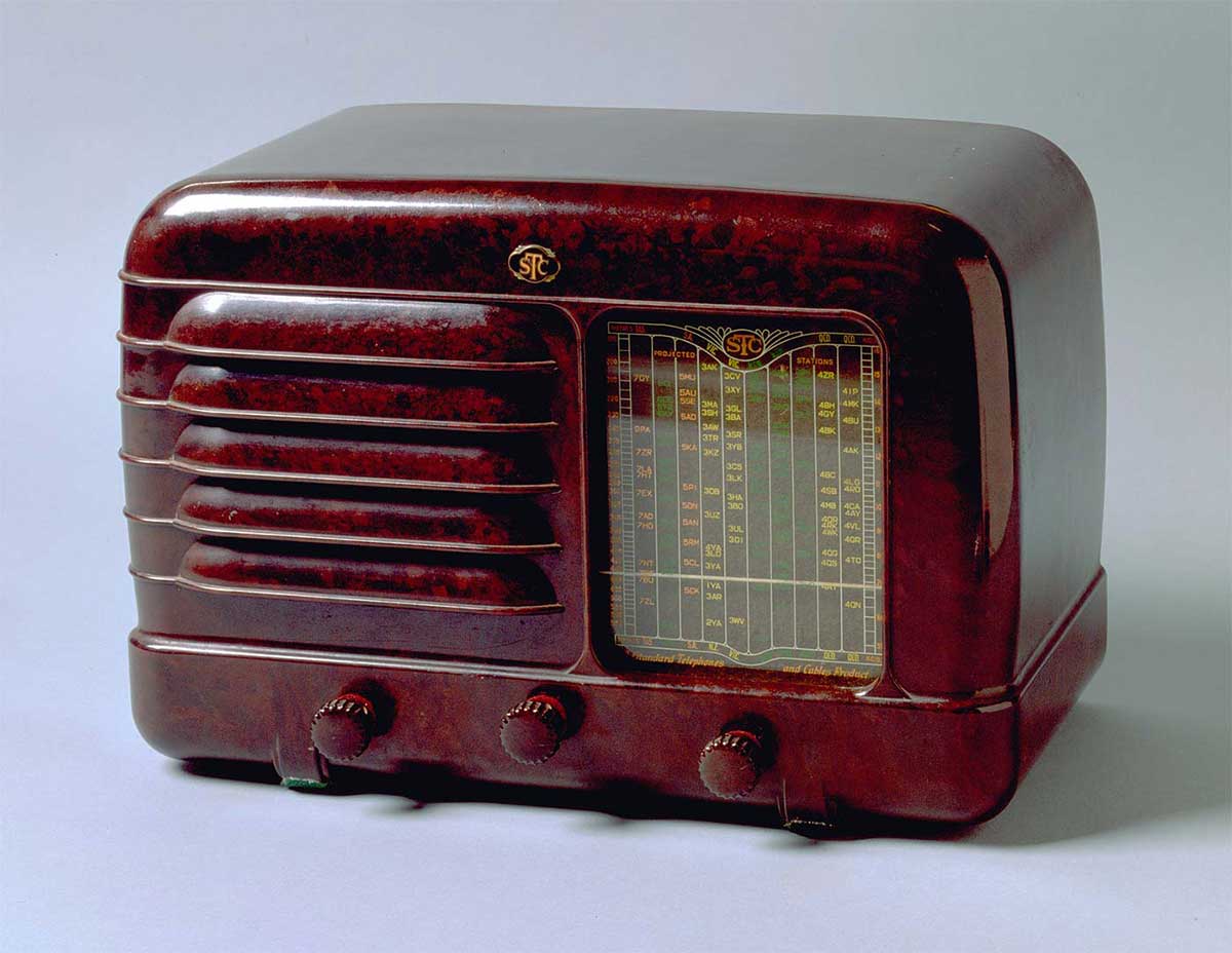 A mantel radio in a deep red colour. The radio face shows three knobs in the lower section, a speaker to the left, and tuner display to the right.  - click to view larger image