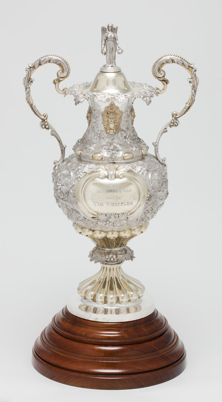 Carved silver trophy with gold inlay and two onate handles mounted on a wooden base. - click to view larger image
