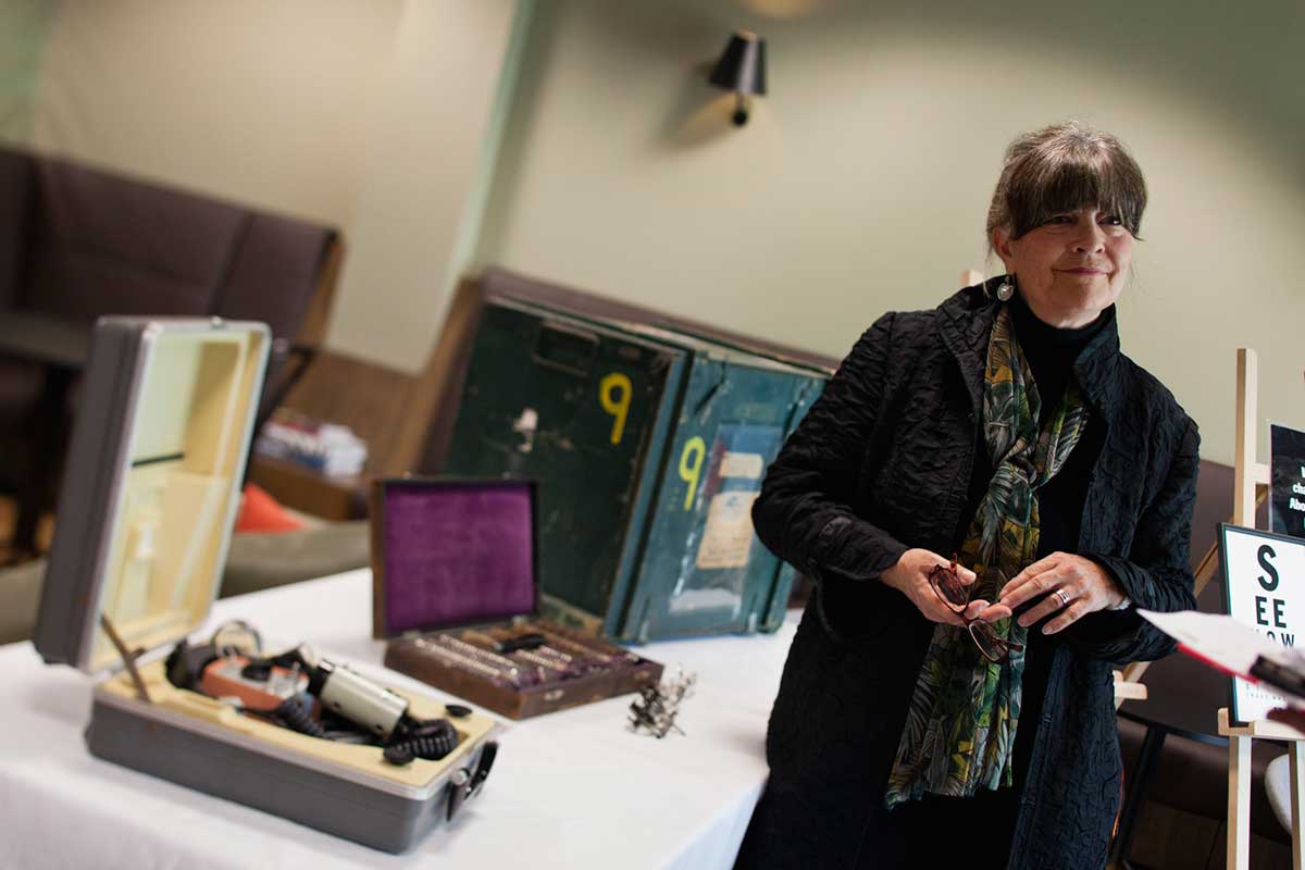 Gabi Hollows stands at right, beside a table where several cases of equipment are displayed. - click to view larger image