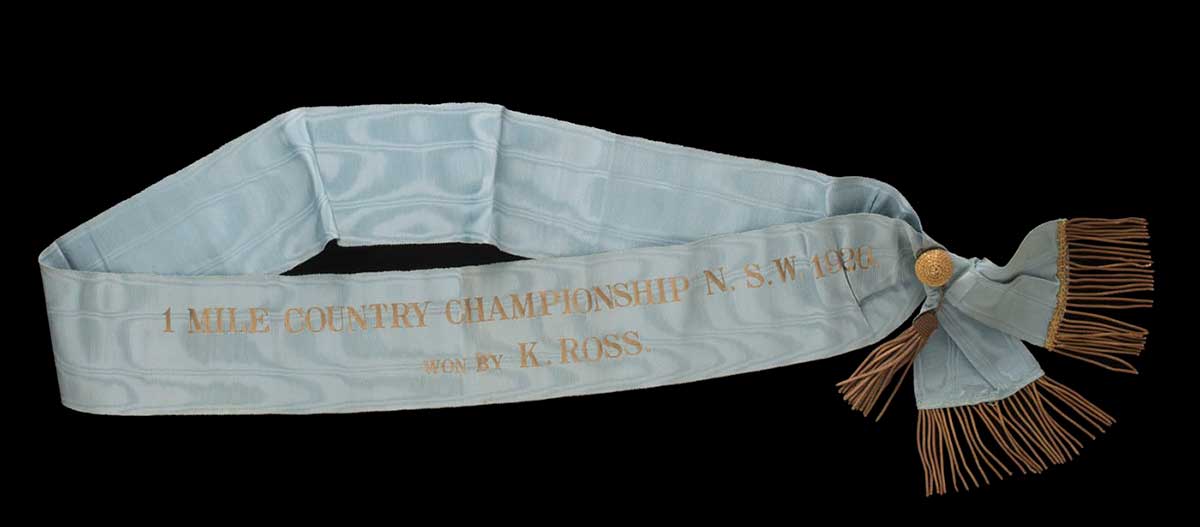 Pale blue ribbed textile sash with gold fringed tassel and gold coloured printed text. - click to view larger image