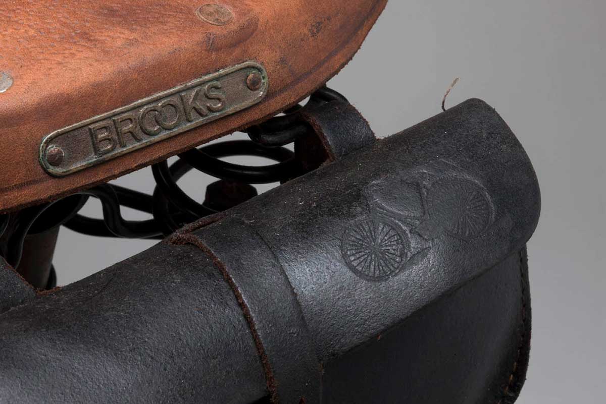 Detail of a bicycle featuring embossed leather bicycle motif on saddle bag and 'Brooks' brand label on seat. - click to view larger image
