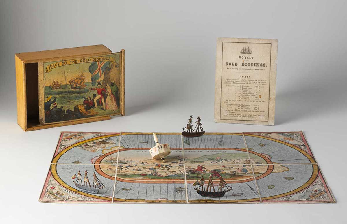 A playing board with three sailing ship markers and a dice, in front of a box with 'RACE TO THE GOLD DIGGINGS' printed on the sliding lid, and a printed rule sheet. - click to view larger image