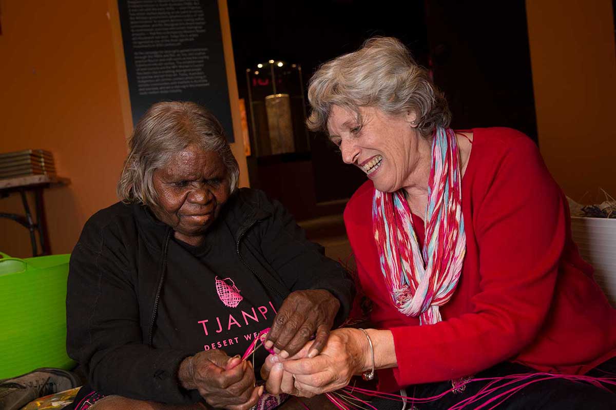 Two women holding strands of a woven object - click to view larger image