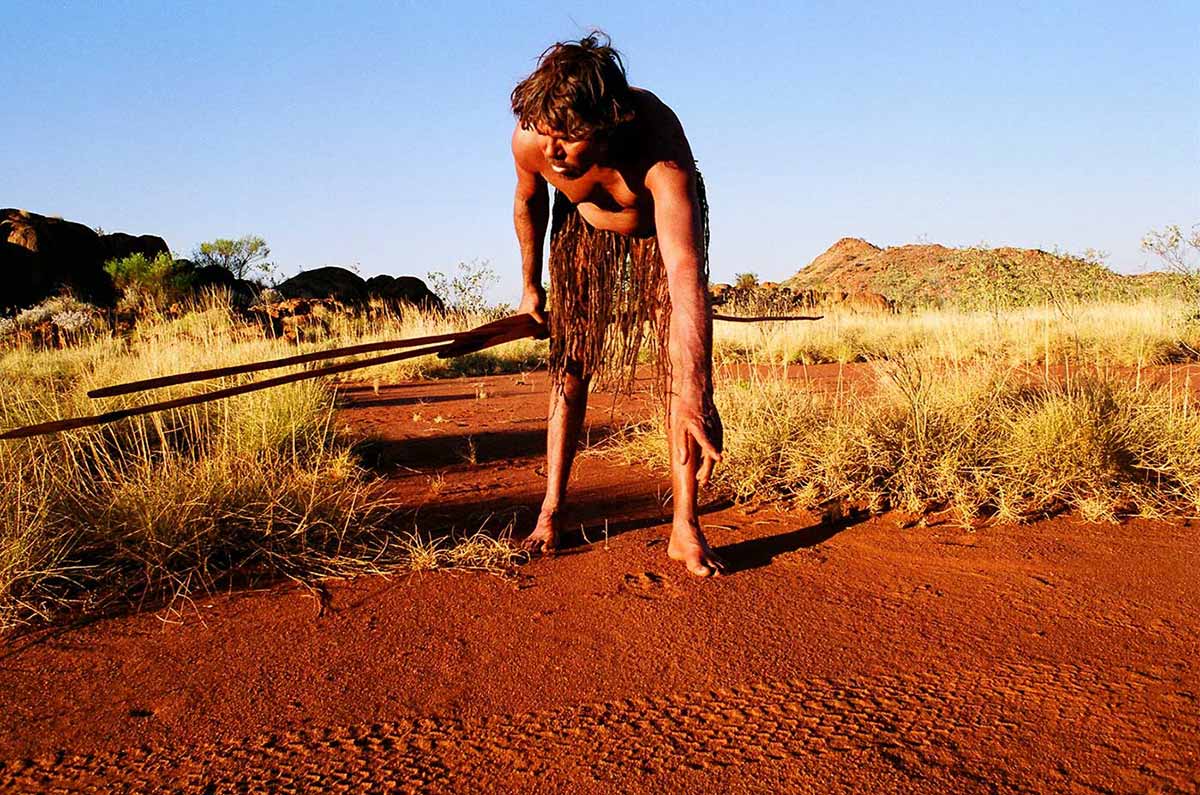 An Aboriginal boy looking a tyre tracks on a red dirt road. - click to view larger image