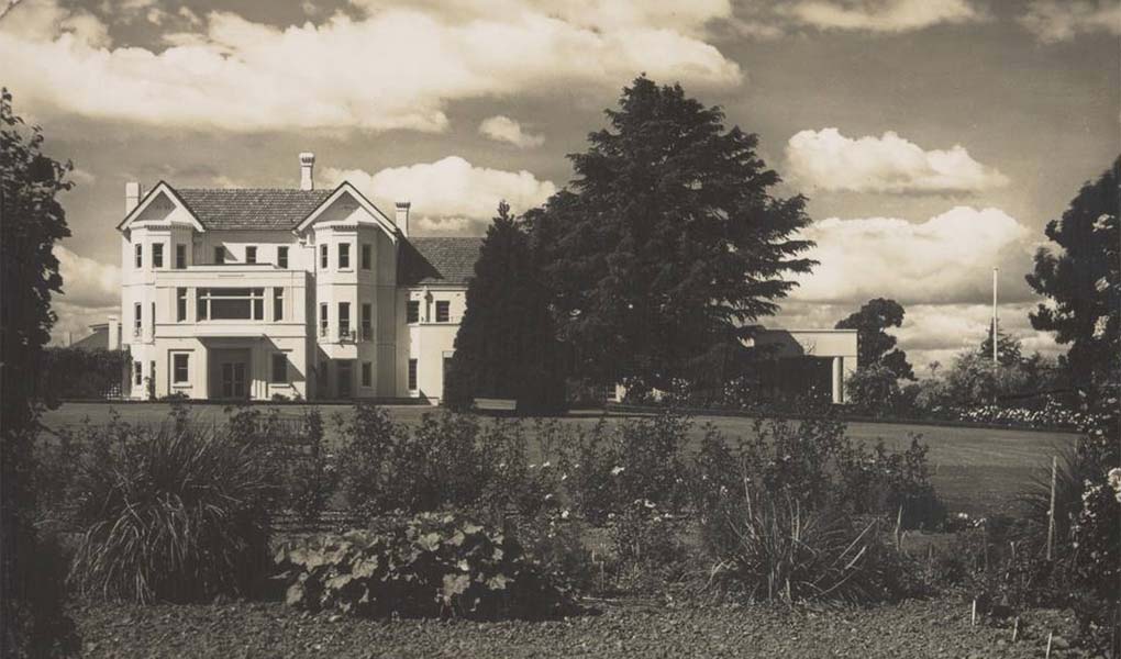 A sepia toned photographic postcard of a grand white  building in sweeping gardens.