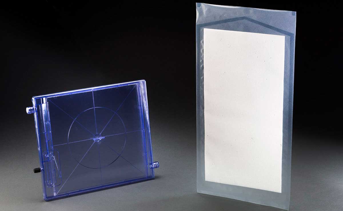 Disposable cassette moulded from specialised medical grade, high flow polycarbonate. It is square and made from purple plastic. Biodegradable Temporising Matrix Dressing in a sealed clear plastic bag. The dressing is a sheet of thin cream coloured foam. - click to view larger image