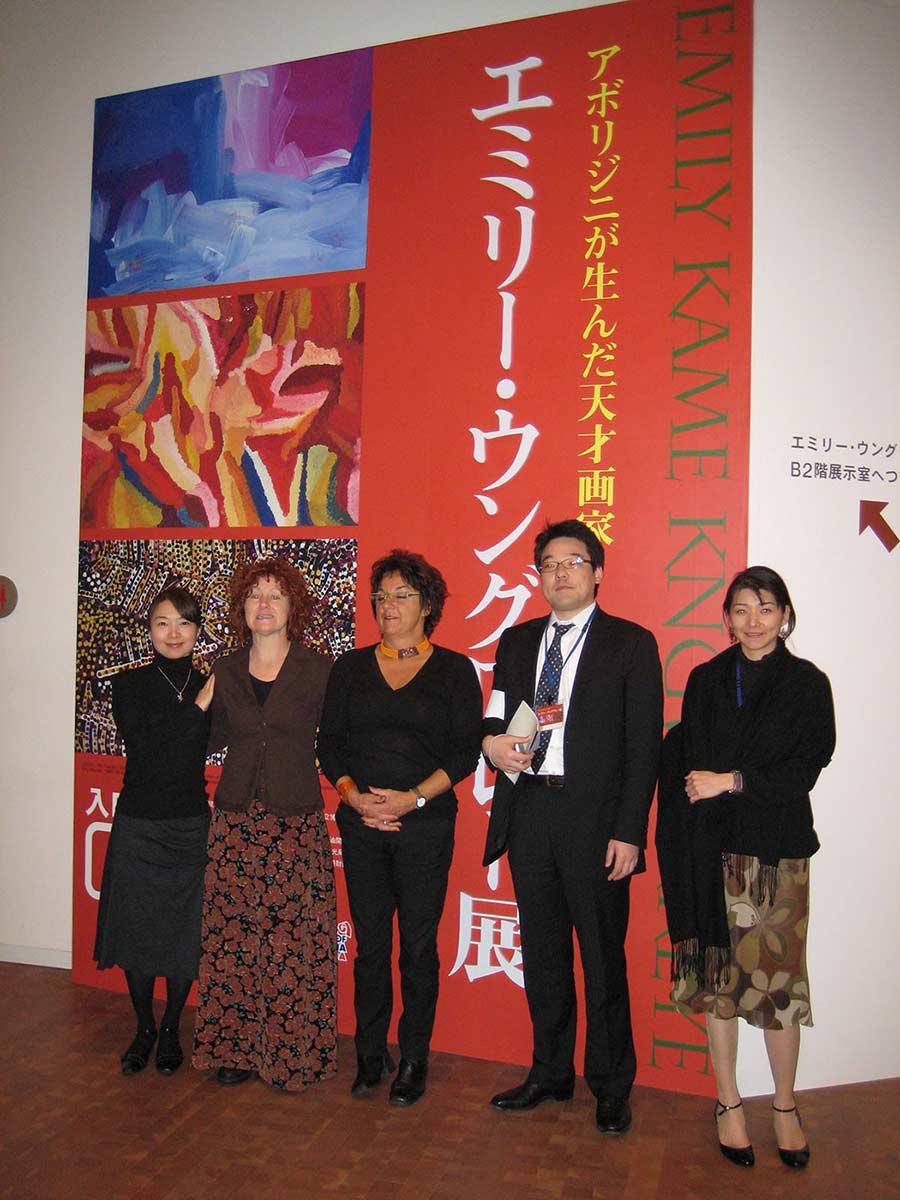 A group of women and a man standing in front of a large exhibition banner. - click to view larger image