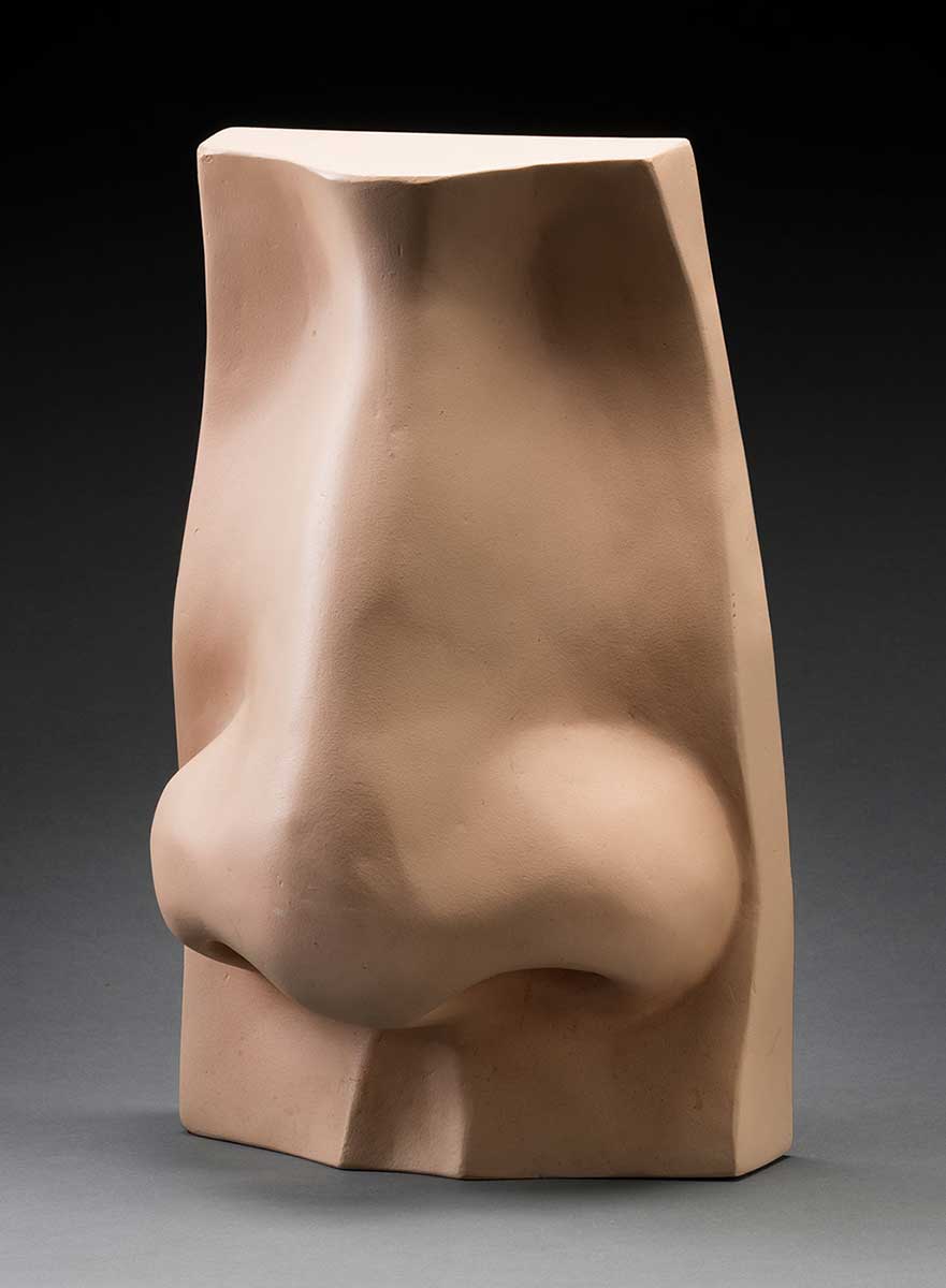 A large scale model of a nose, which is flesh coloured, and hollow at the back. The surface of the model is damaged in the proper left nostril, and a piece is missing. - click to view larger image