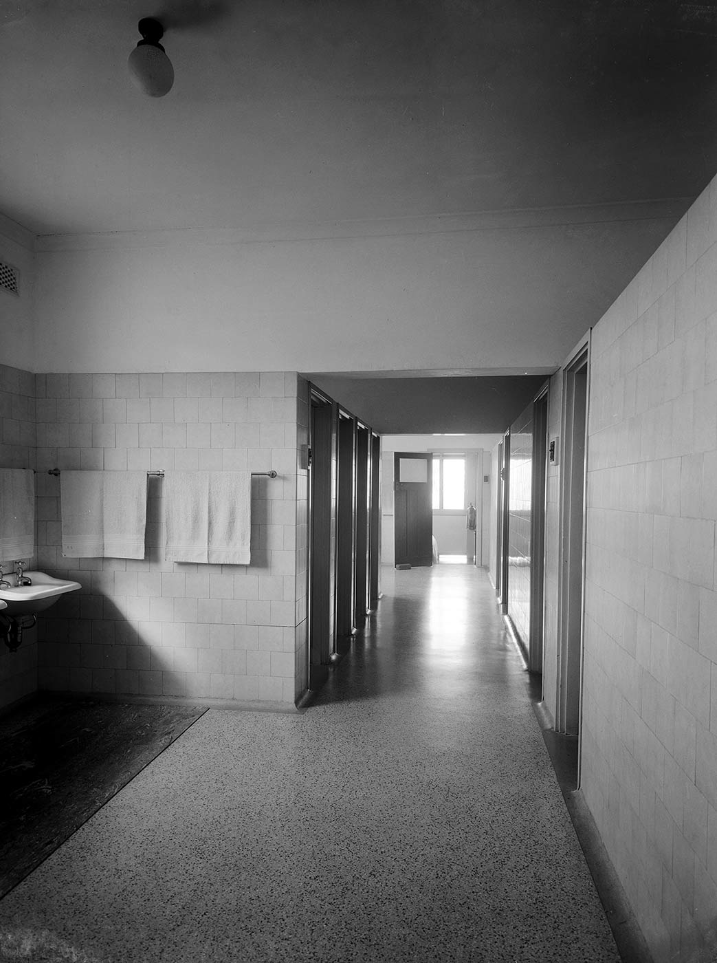 Image showing a long corridor, with a sink and towels on the left, several doorways in the centre and an open door at the far end. - click to view larger image