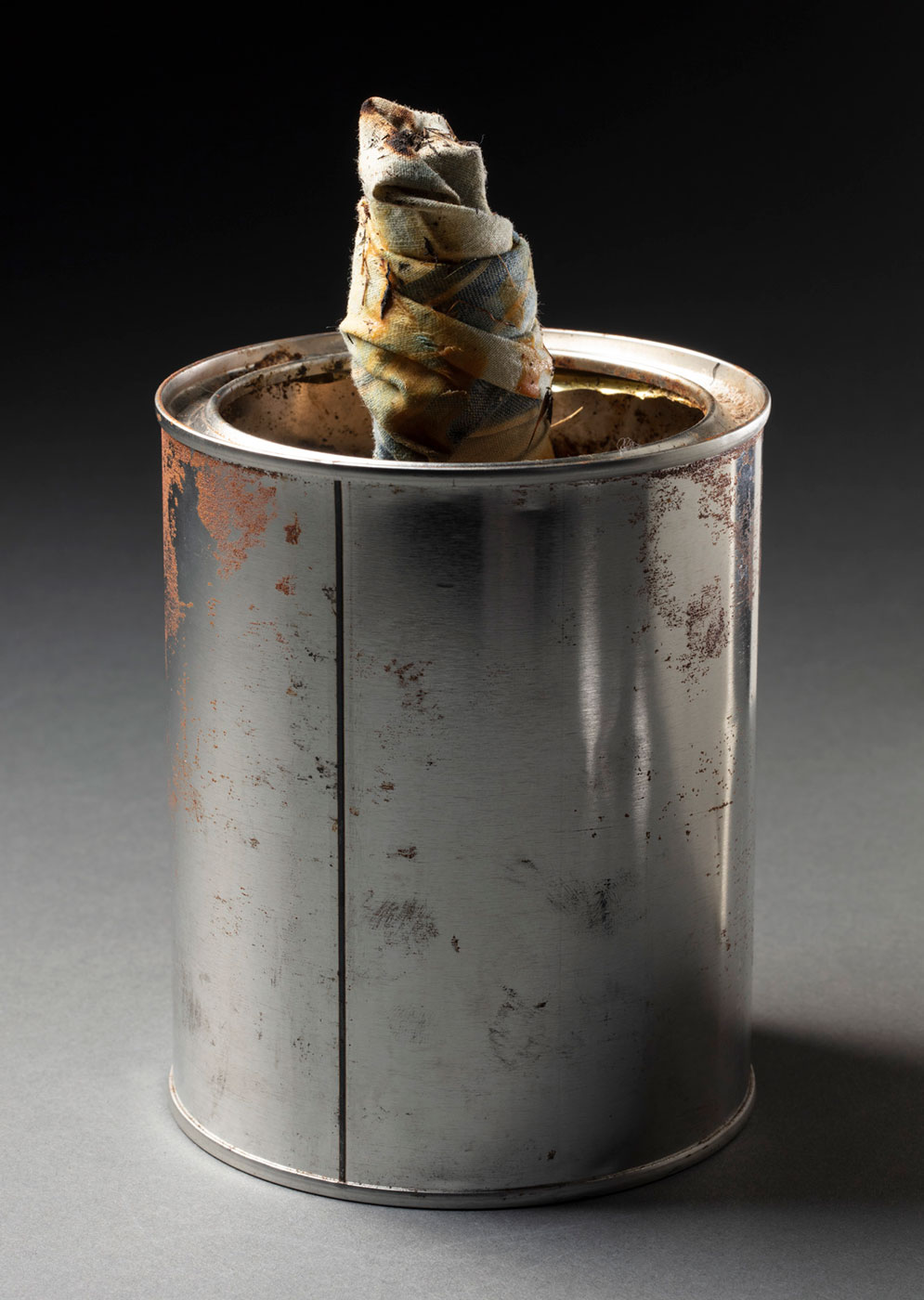 Lamp consisting of a metal tin holding a wick made from a twisted piece of blue and fabric . - click to view larger image