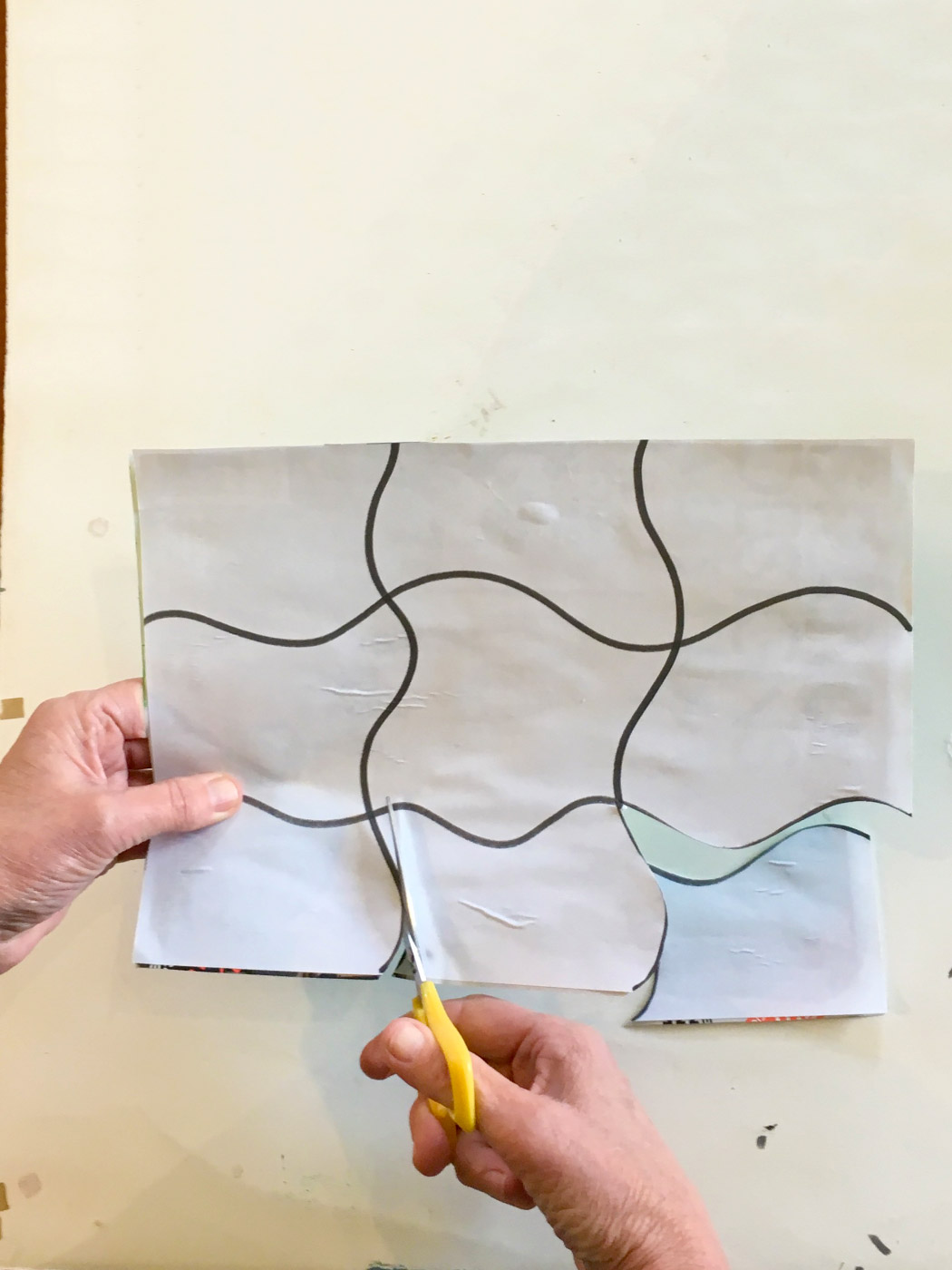 A pair of hands cutting along the lines of a template for a jigsaw puzzle.